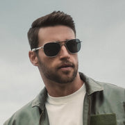 Pilot wearing aviator sunglasses and a green flight jacket against a gray background