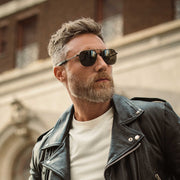 Pilot  wearing Aviator Military Special Edition Matte Black sunglasses and a leather jacket in an urban setting