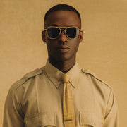 Pilot wearing a beige uniform and Class A Aviator - Desert Sand & American Gray sunglasses against a beige background